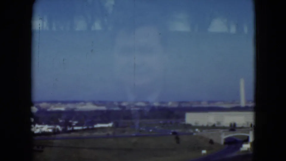 1975 8mm closing frame with a distant Washington Monument view and low building seen through the vehicle window.