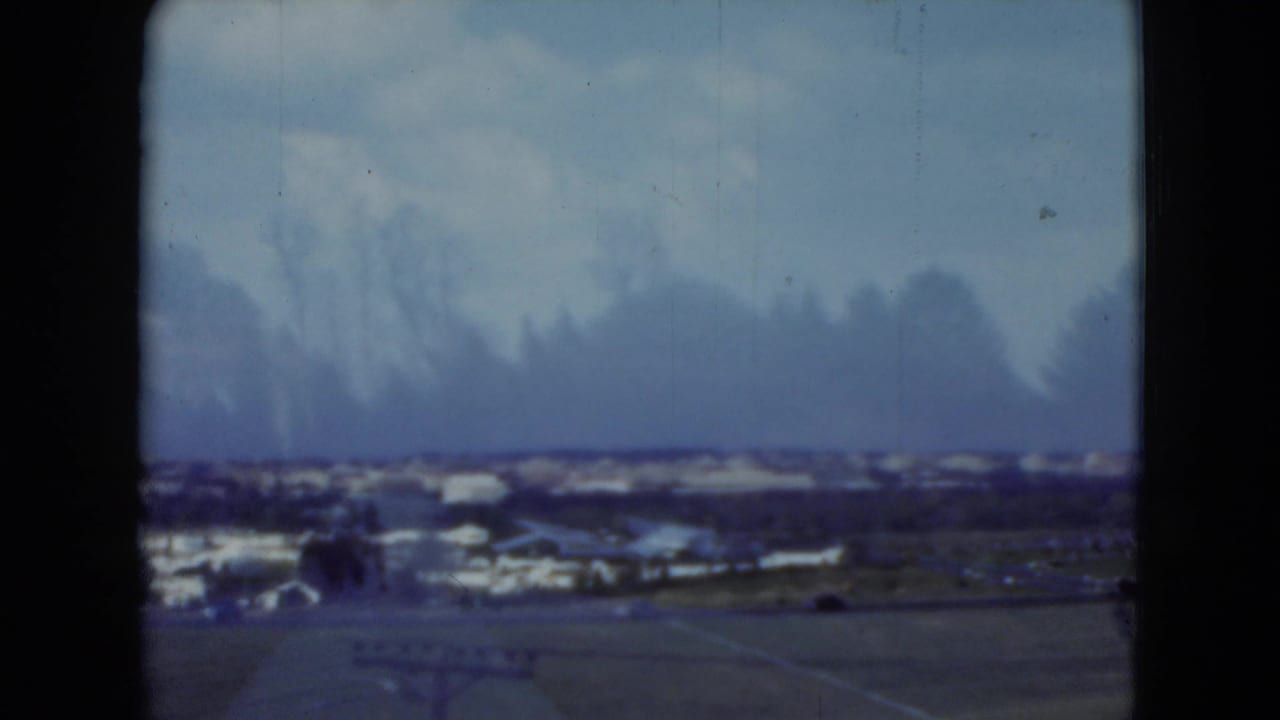 Elevated 1975 Middletown, Pennsylvania view with low buildings, open ground, distant roads, and a hazy blue sky.