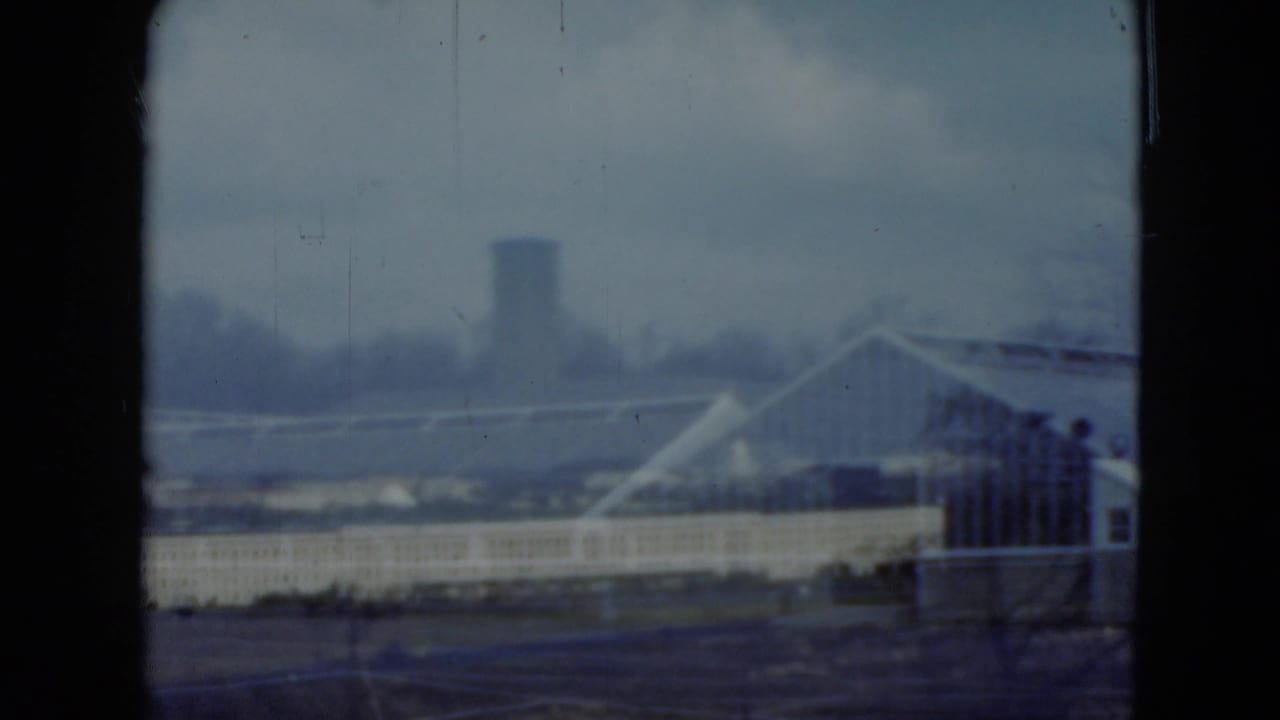 1975 Middletown, Pennsylvania view toward a white industrial building, roof trusses, and a distant vertical tower in soft focus.