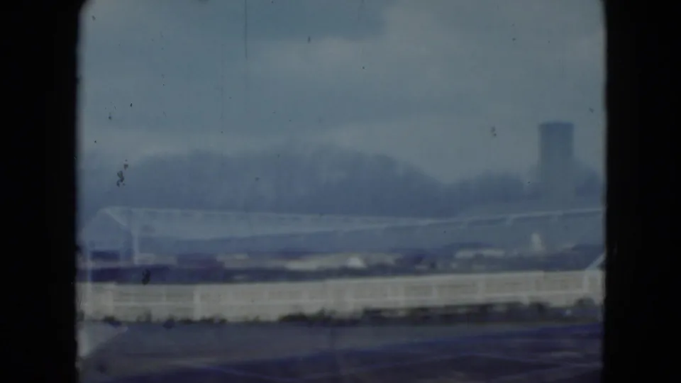 Blurred 8mm frame of the Middletown industrial area, showing a long pale building and a tower beyond the roofline.