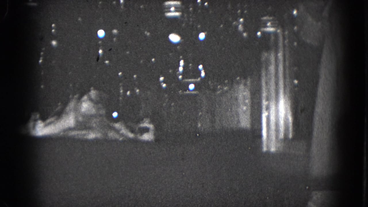1975 Middletown, Pennsylvania 8mm frame showing a dim home Christmas display with mantel sign, ornament, and dark background reflections.