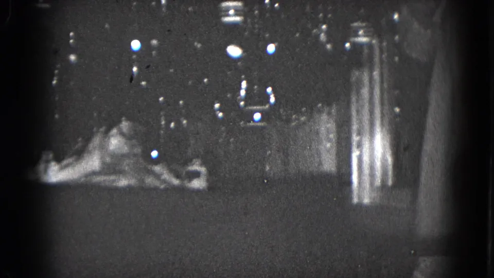 1975 Middletown, Pennsylvania 8mm frame showing a dim home Christmas display with mantel sign, ornament, and dark background reflections.