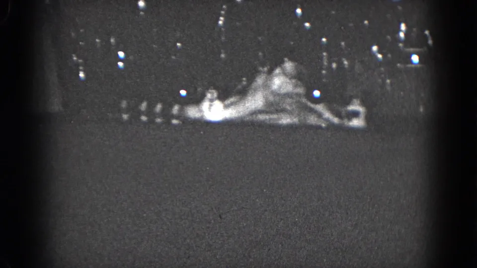 1975 8mm home-movie frame from Middletown showing a reclining holiday figure or ornament above a dim mantel display.