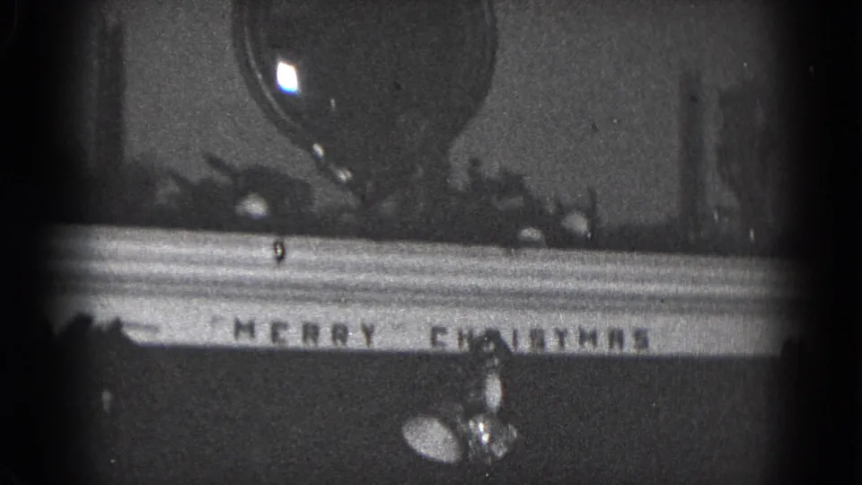 1975 Middletown 8mm frame showing the lower mantel area with a Merry Christmas sign, shiny ornament, and small holiday pieces.