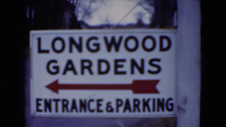 1975 Pennsylvania home-movie frame showing a closer view of the Longwood Gardens entrance and parking sign.