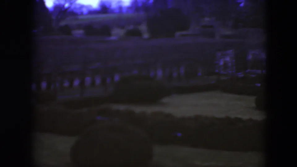 Dark 1975 8mm frame from Middletown, Pennsylvania, showing a formal garden area with hedges, a path and a railing under heavy color shift.