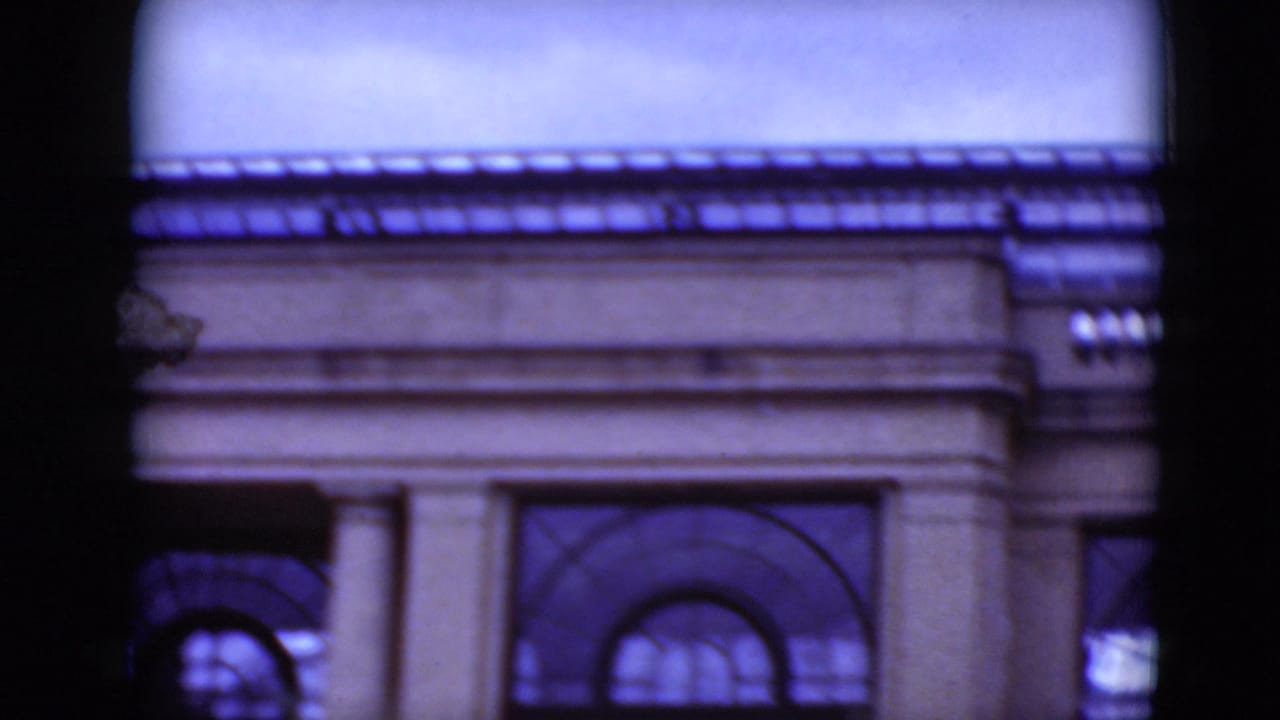 Upper portion of a classical facade with columns, arched windows and roof trim.