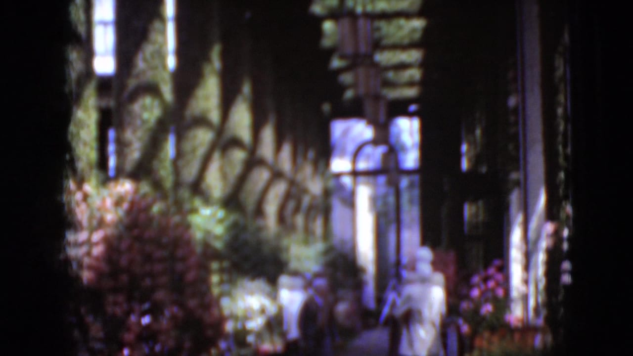 1975 Middletown, Pennsylvania home-movie frame showing visitors along a church-side path with arched windows and flowers.