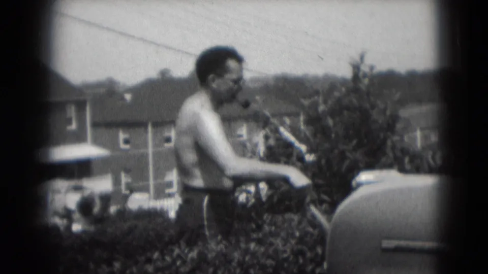 1975 Middletown, Pennsylvania frame showing an adult man with glasses near a car and shrubs in a residential yard.