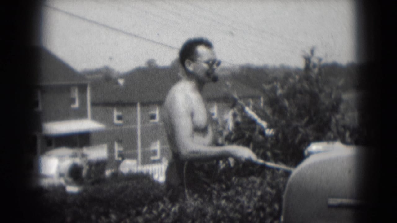 In Middletown, Pennsylvania in 1975, a shirtless man smokes a large cigar while standing by a backyard grill.