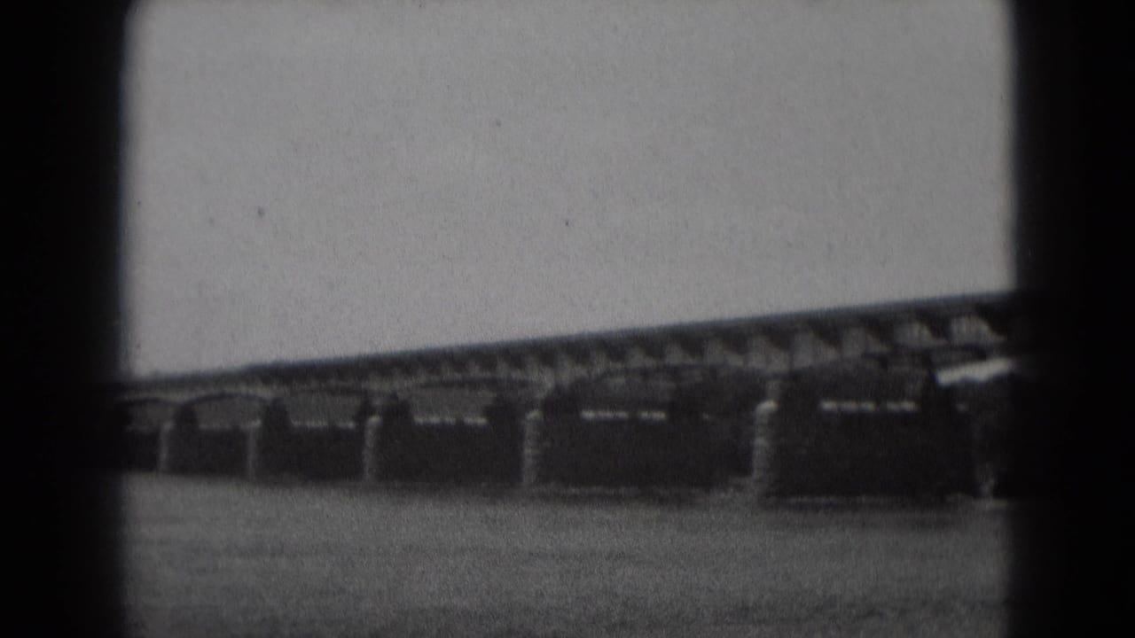 Long bridge span with stone supports over water, seen through dark 8mm frame edges.
