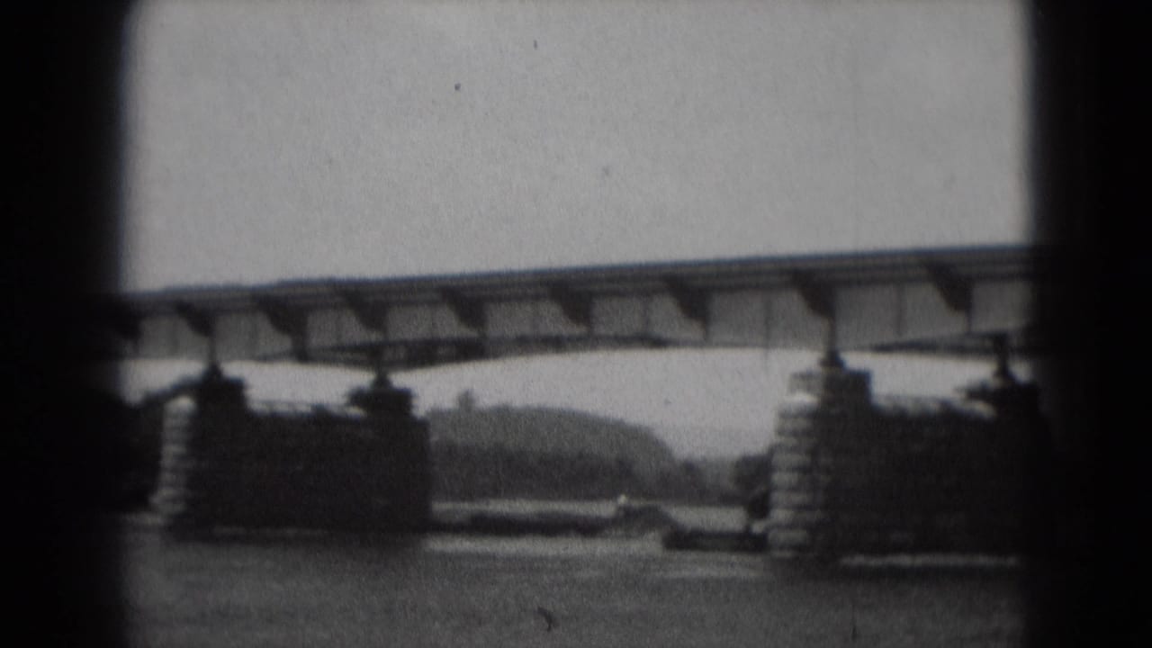 1975 Middletown, Pennsylvania 8mm frame showing a metal bridge crossing a river on large piers, with wooded banks beyond.