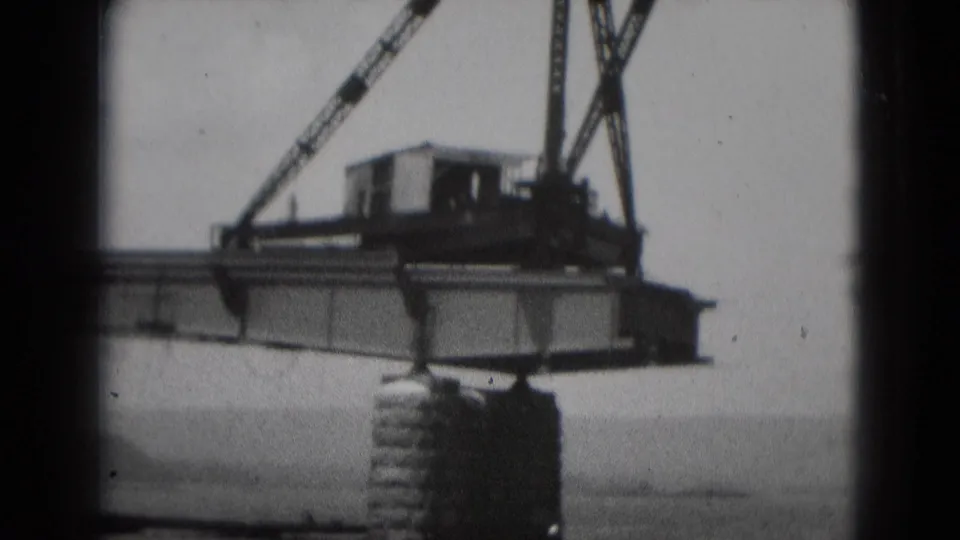 Black-and-white 8mm view of the crane and suspended beam at a Middletown construction area in 1975.
