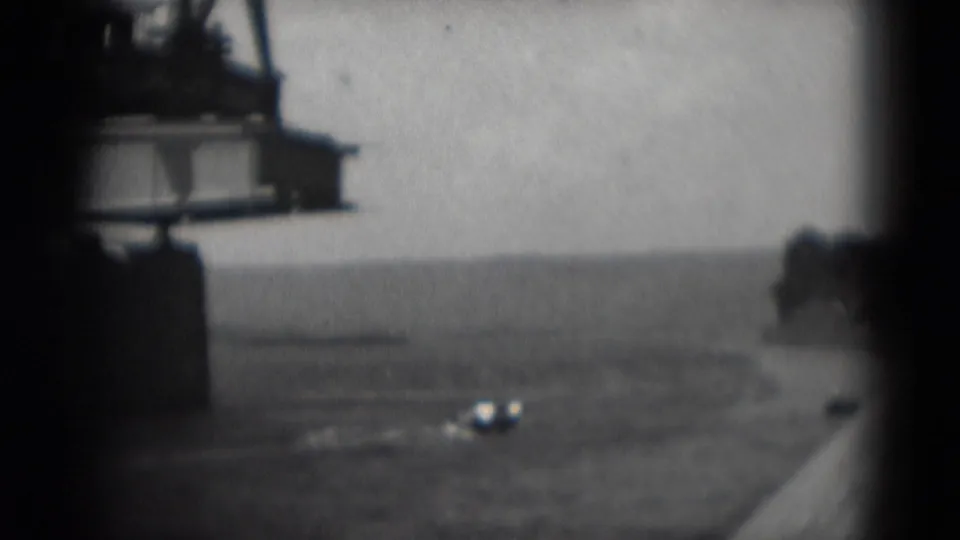 The boat continues across the water as the construction span and pier edge remain partly visible in the home-movie frame.
