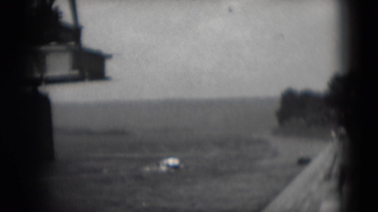 Grainy 1975 8mm view of an industrial crane beside the river in Middletown, Pennsylvania, with a small boat in the distance.