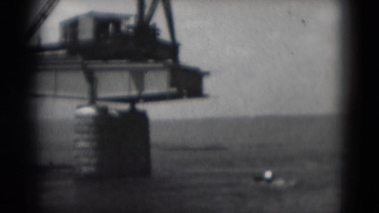 Crane structure beside open water with a small bright boat to the right.