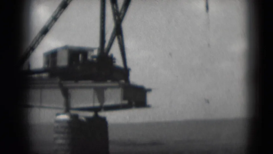 Soft 8mm frame from Middletown in 1975 showing a crane cab, platform, and riverside industrial edge against open water.