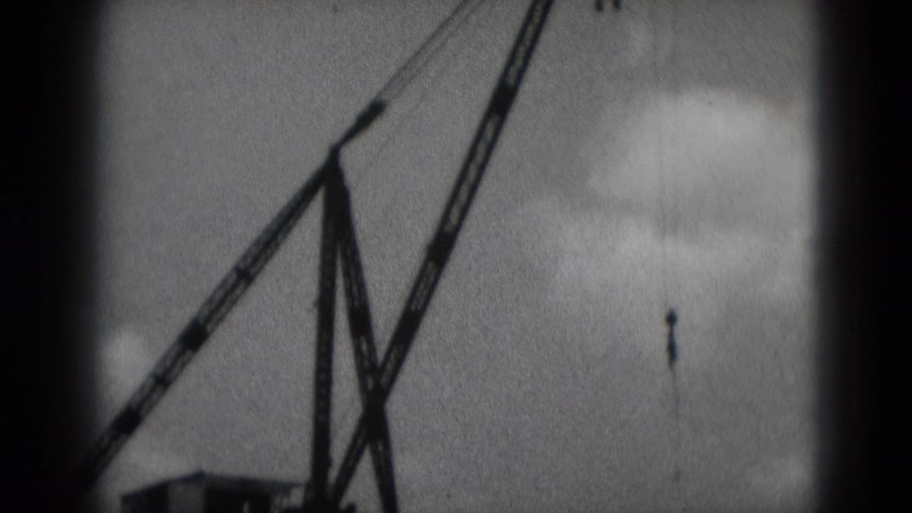 Lattice-boom crane angled against a cloudy sky with dark film borders.