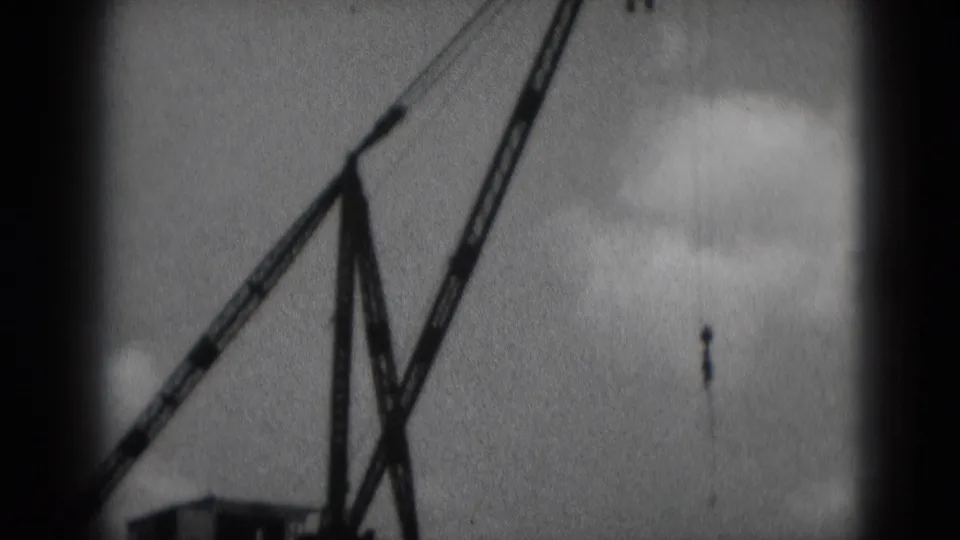 1975 Middletown, Pennsylvania 8mm frame showing a crane boom and hanging hook against a cloudy sky.