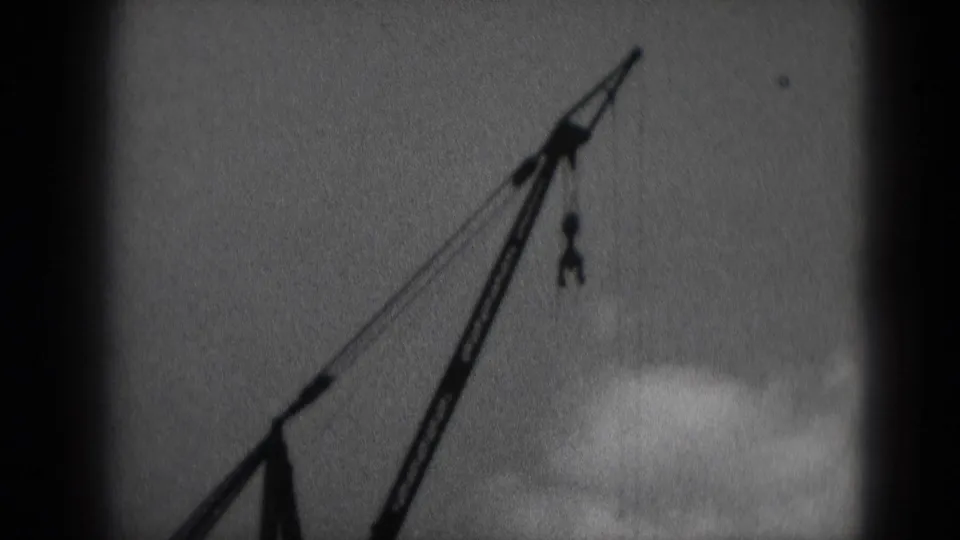 1975 Middletown, Pennsylvania frame of an industrial crane boom and hook seen through grainy 8mm film.