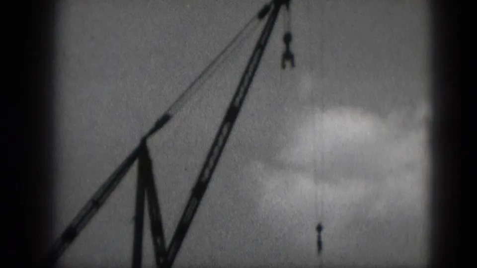 Grainy 8mm view of a crane boom and suspended hook at a Middletown, Pennsylvania construction site in 1975.