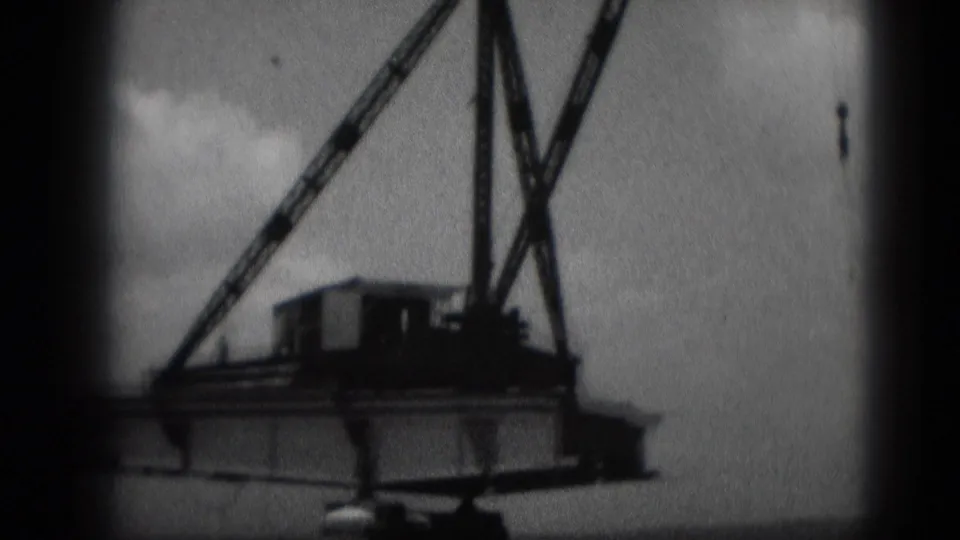 1975 Middletown, Pennsylvania 8mm frame showing a crane body, raised boom, and hanging hook at a construction site.