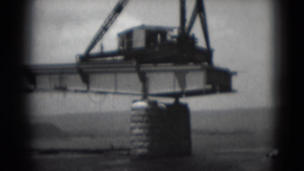 Bridge deck and equipment above a concrete support with water in the background.