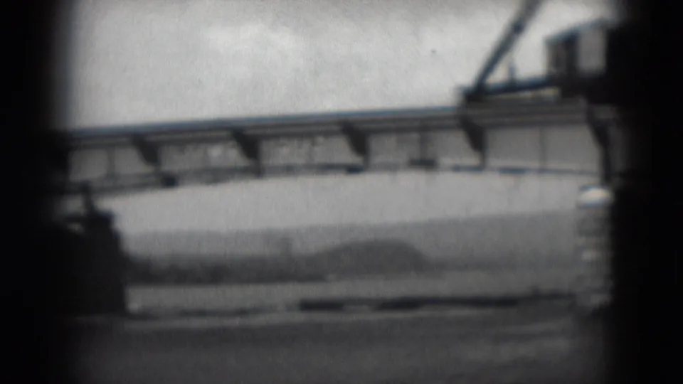 Soft black-and-white 8mm frame of a long bridge span over water near Middletown, Pennsylvania, with support structure and shoreline visible.