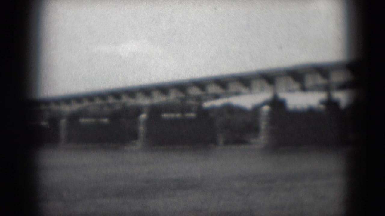 Bridge crossing water with dark foreground framing and low shoreline beyond.