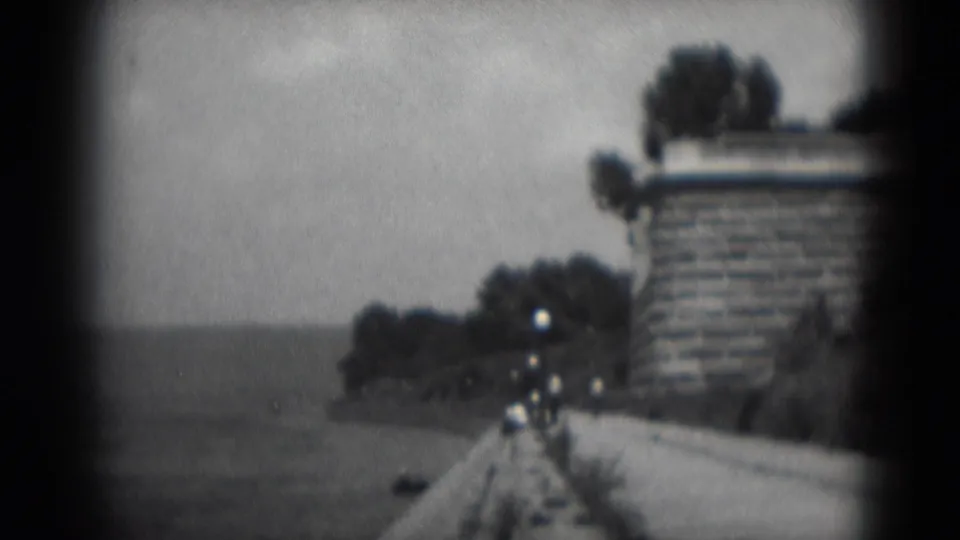 Black-and-white 8mm frame from Middletown, Pennsylvania, showing a waterside path, stone wall, trees and small distant figures walking.