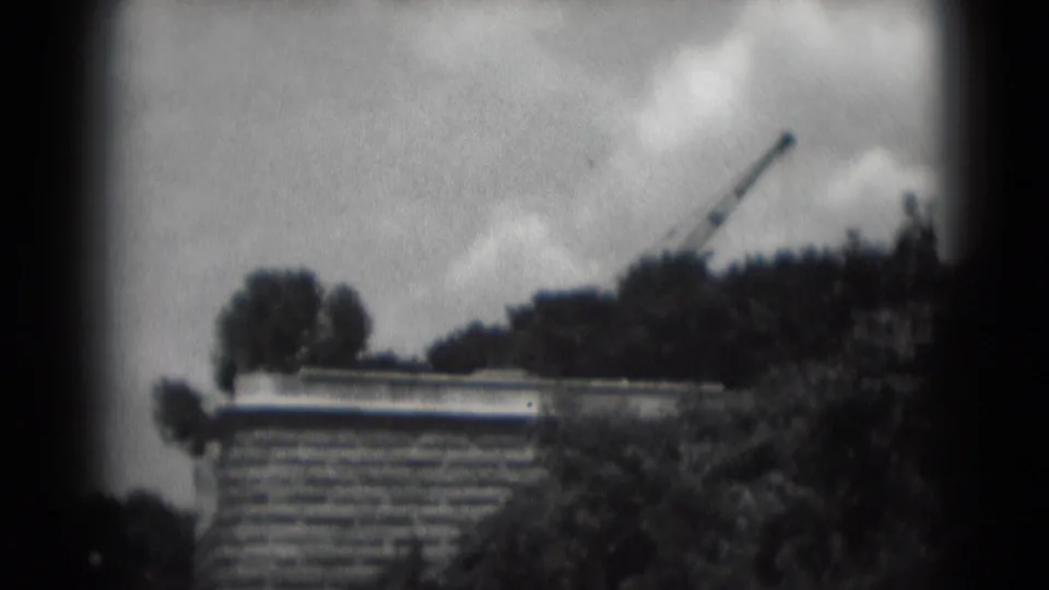 1975 Middletown, Pennsylvania 8mm frame showing a brick building edge, treetops, cloudy sky, and a crane in the distance.