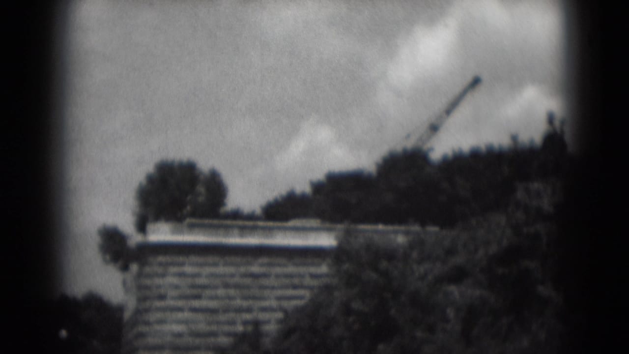 Soft view of a brick building, trees, clouds, and crane above the skyline.