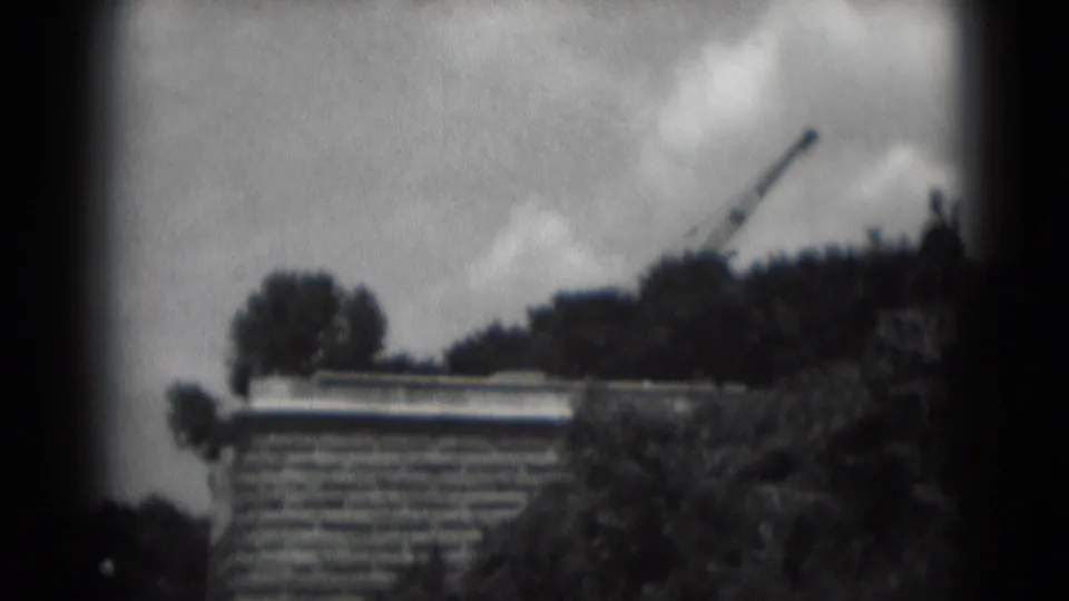 Soft 8mm view in Middletown, Pennsylvania, with a brick building below trees and a construction crane against clouds.
