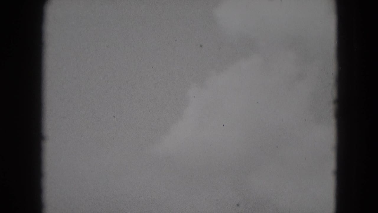 Pale gray sky with soft cloud shapes and dark film borders.