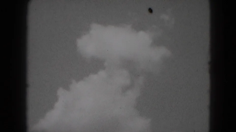 1975 Middletown sky frame with a large white cloud mass against gray sky, seen through grainy 8mm film edges.