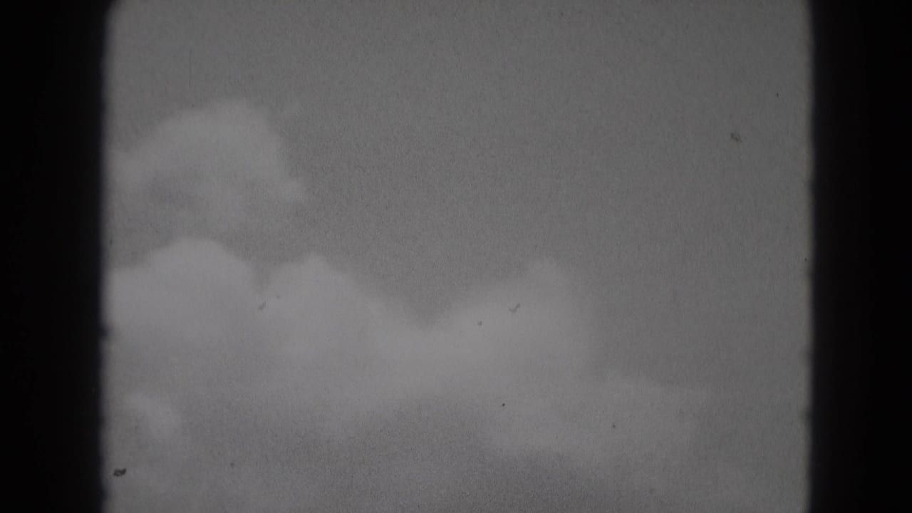 Soft clouds across a pale sky with dark film edge at left.