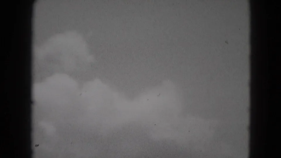 1975 Middletown, Pennsylvania 8mm frame showing soft cloud forms in a pale sky with grain, dust, and a dark vertical frame edge.