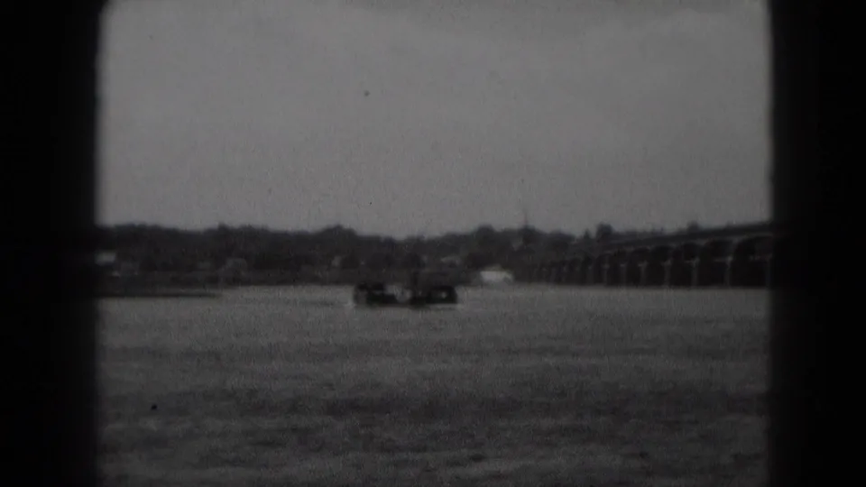 1975 Middletown, Pennsylvania 8mm frame showing a distant river, low shoreline, long bridge, cloudy sky, and dark film borders.