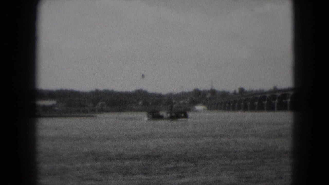 Distant boat on a wide river with an arched bridge at right.