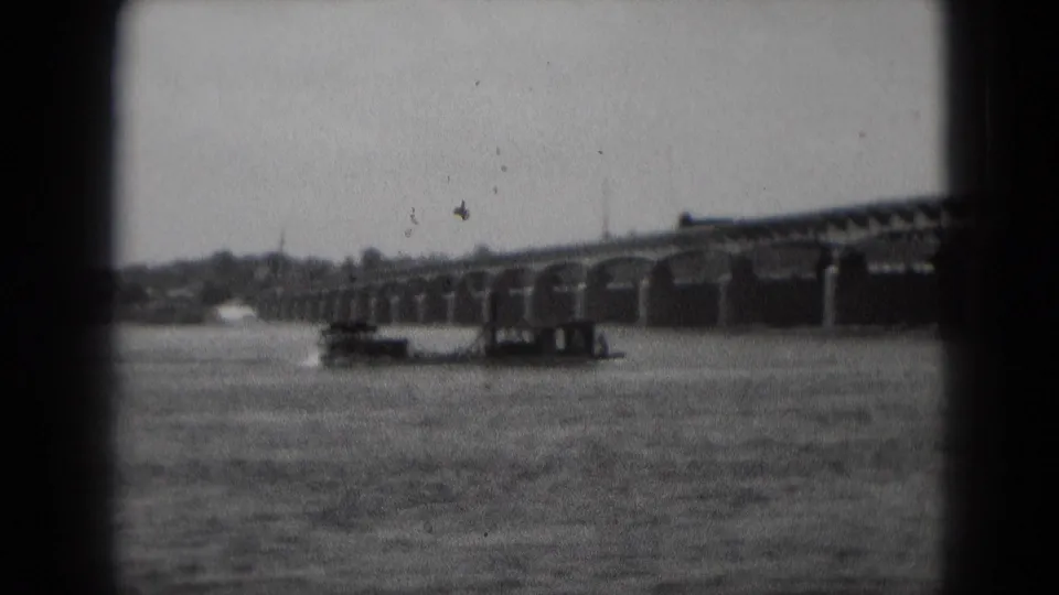 A river boat sits near the bridge piers as repeating arches cross the frame in 1975 black-and-white 8mm footage.