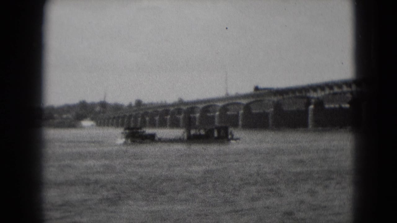 1975 8mm frame from Middletown, Pennsylvania, showing a paddle boat on rippled water near a long arched bridge.