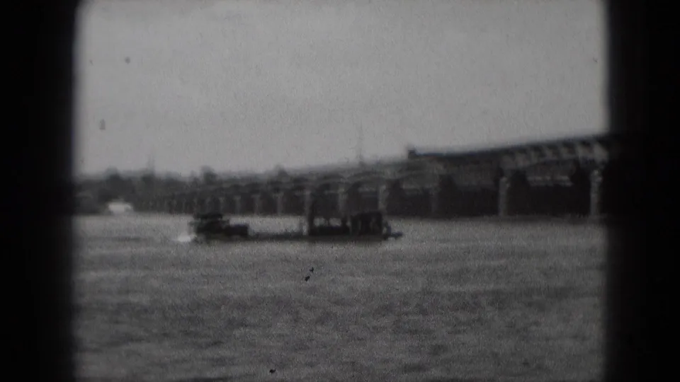 Black-and-white 8mm frame of a paddle boat traveling across water near a long bridge in Middletown, Pennsylvania.