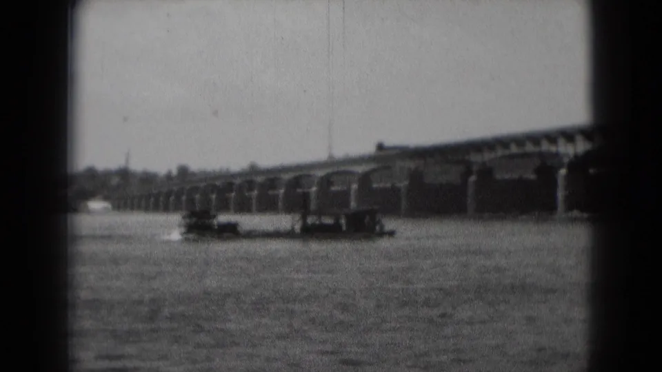 Soft 8mm frame showing the paddle boat closer in the foreground water, with the arched bridge stretching behind it.