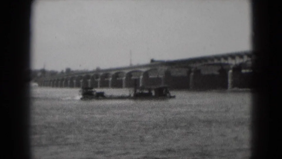 1975 8mm frame from Middletown, Pennsylvania, showing a small barge or workboat on the river beneath a long stone arch bridge.