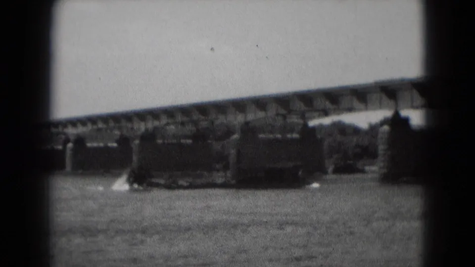 A closer black-and-white 8mm view shows the barge or workboat near the bridge structure, with wake visible on the water.