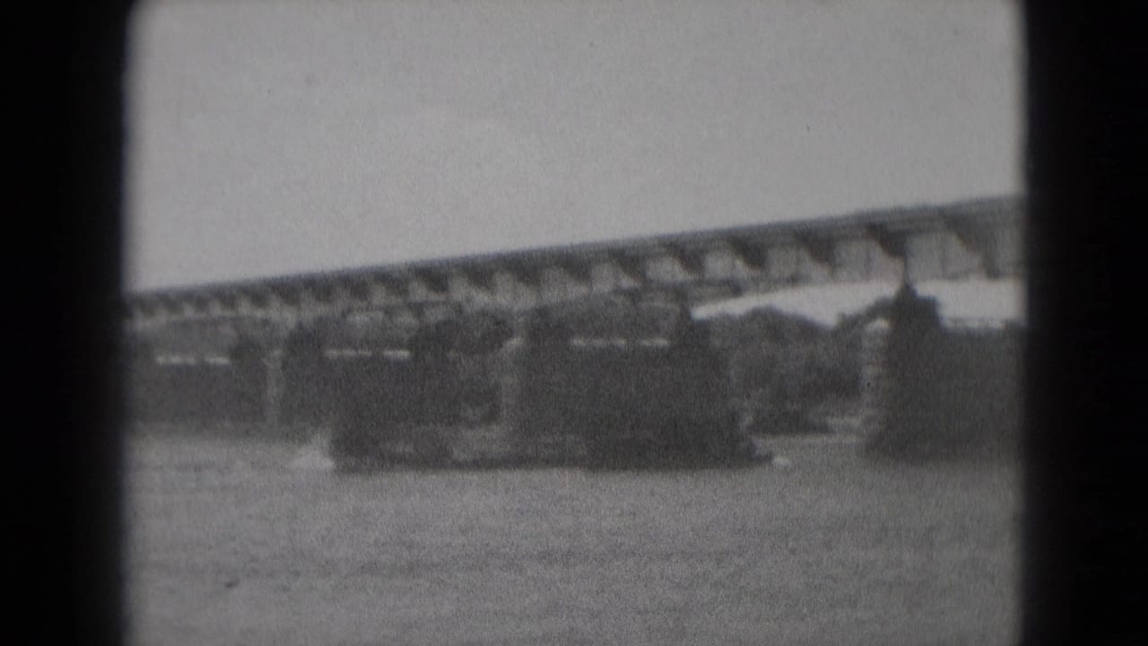 Large dark vessel on a river beneath a long bridge, framed by black 8mm film borders.