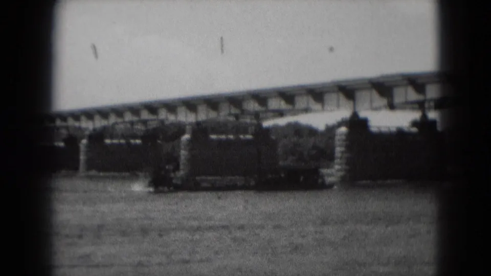A large dark boat continues under or near the bridge in black-and-white 8mm footage from the supplied 1975 Middletown setting.