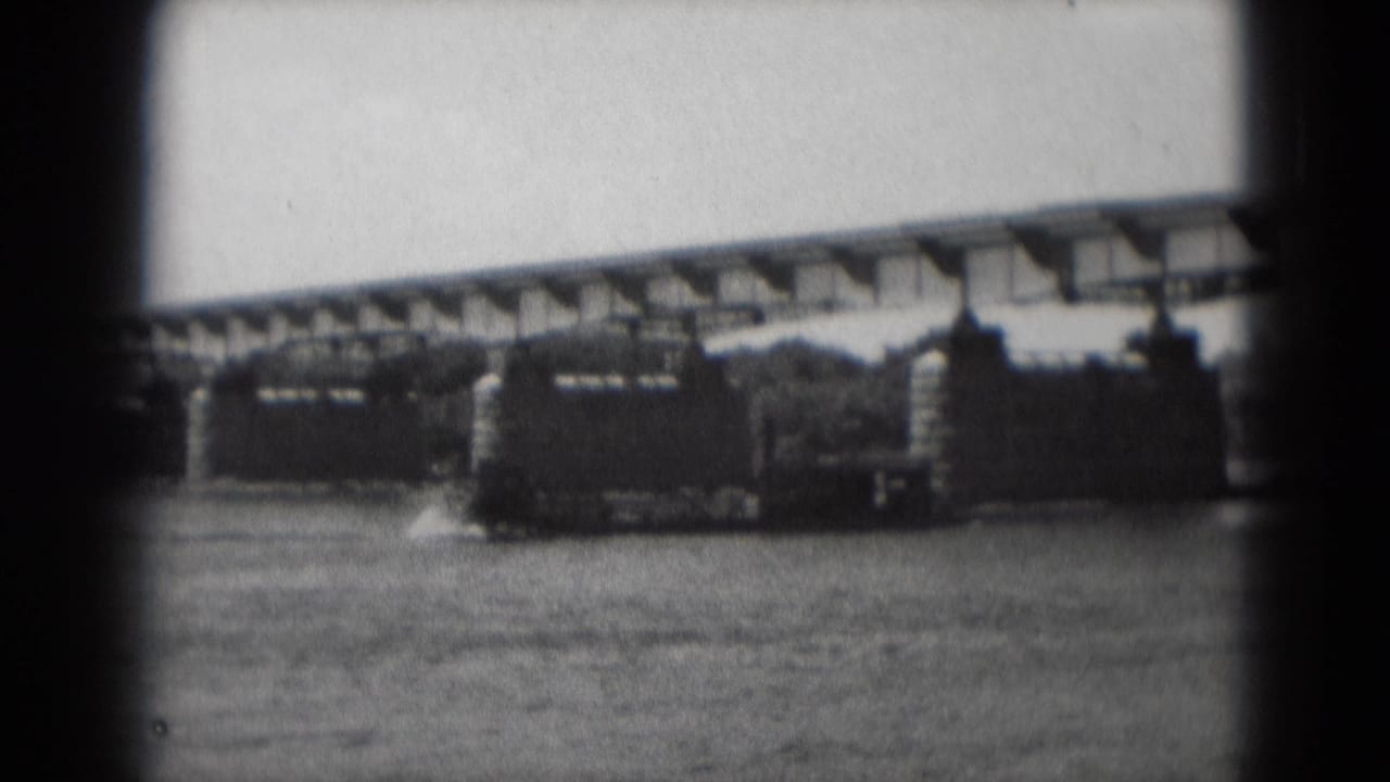 Sternwheeler boat moving on a river beneath a long bridge.