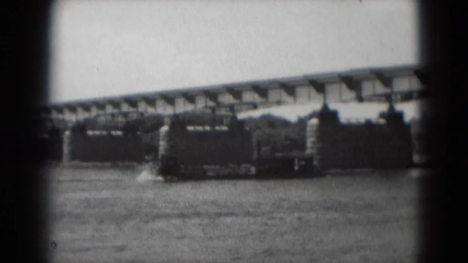 1975 Middletown, Pennsylvania home-movie frame showing a sternwheeler-style boat passing under a long bridge on the river.