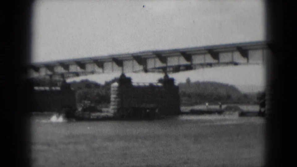 Bridge construction over a river in the supplied 1975 Middletown context, with a crane lifting materials near the unfinished span.